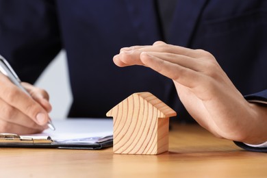 Photo of Property insurance. Real estate agent protecting house figure while working at wooden table, closeup