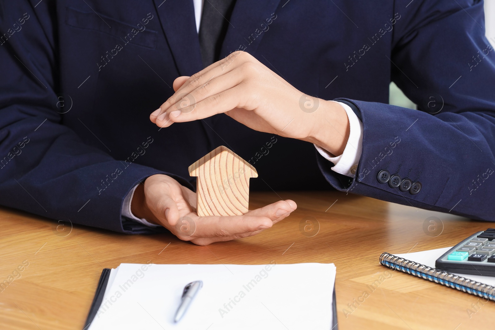 Photo of Property insurance. Real estate agent protecting house figure at wooden table, closeup