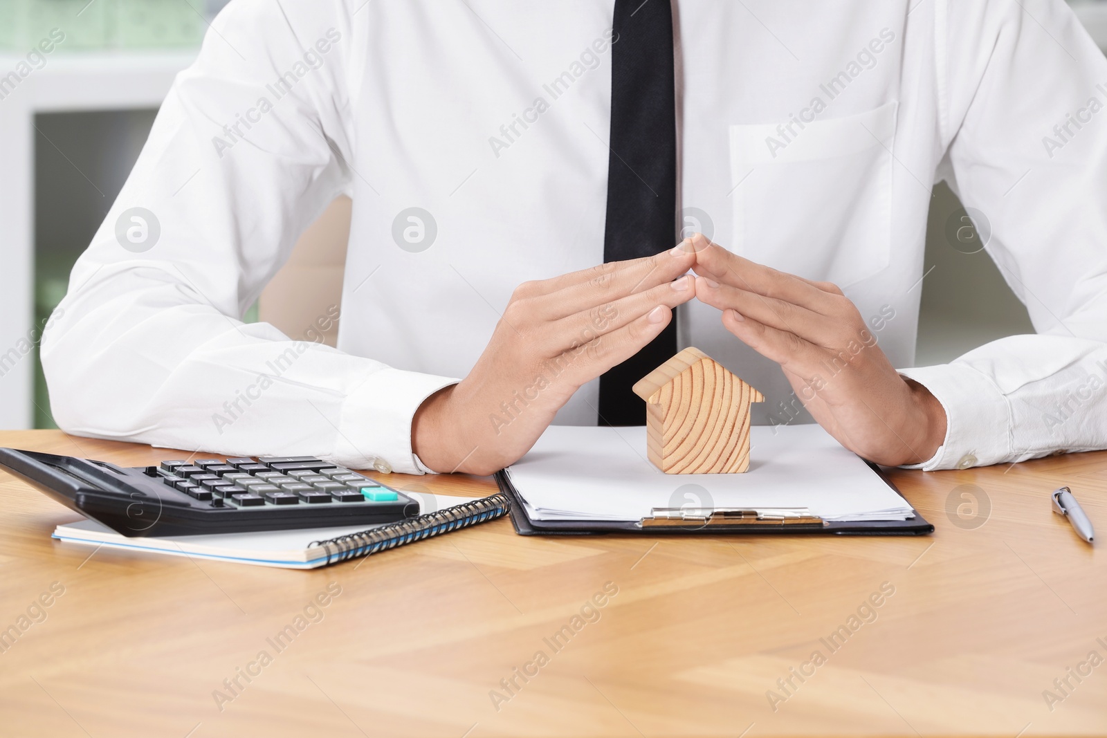 Photo of Property insurance. Real estate agent protecting house figure at wooden table, closeup