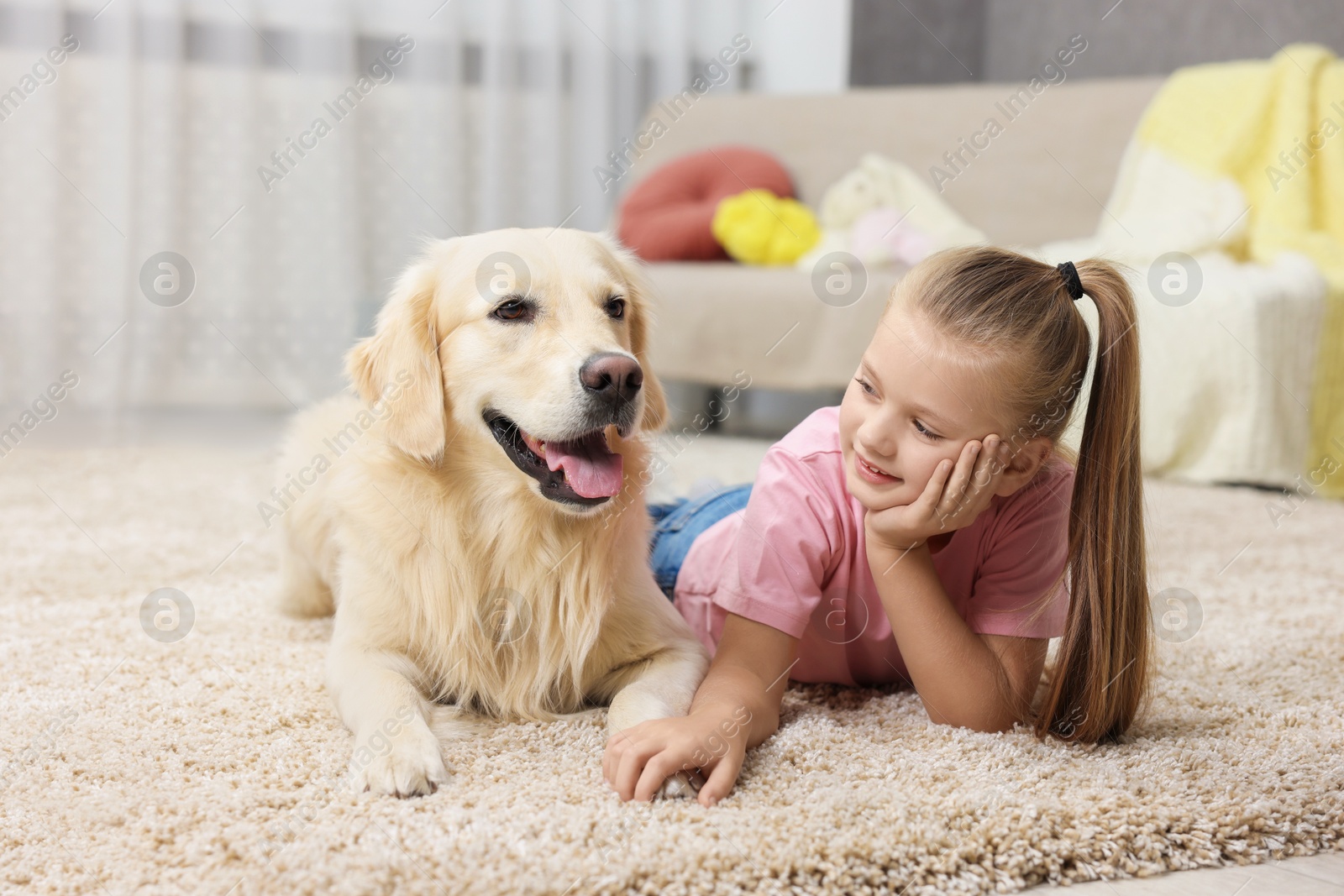 Photo of Girl with cute Golden Retriever dog lying on rug at home