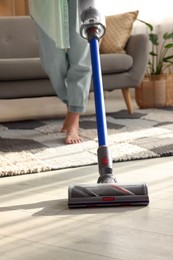 Photo of Woman cleaning floor with cordless vacuum cleaner at home, closeup