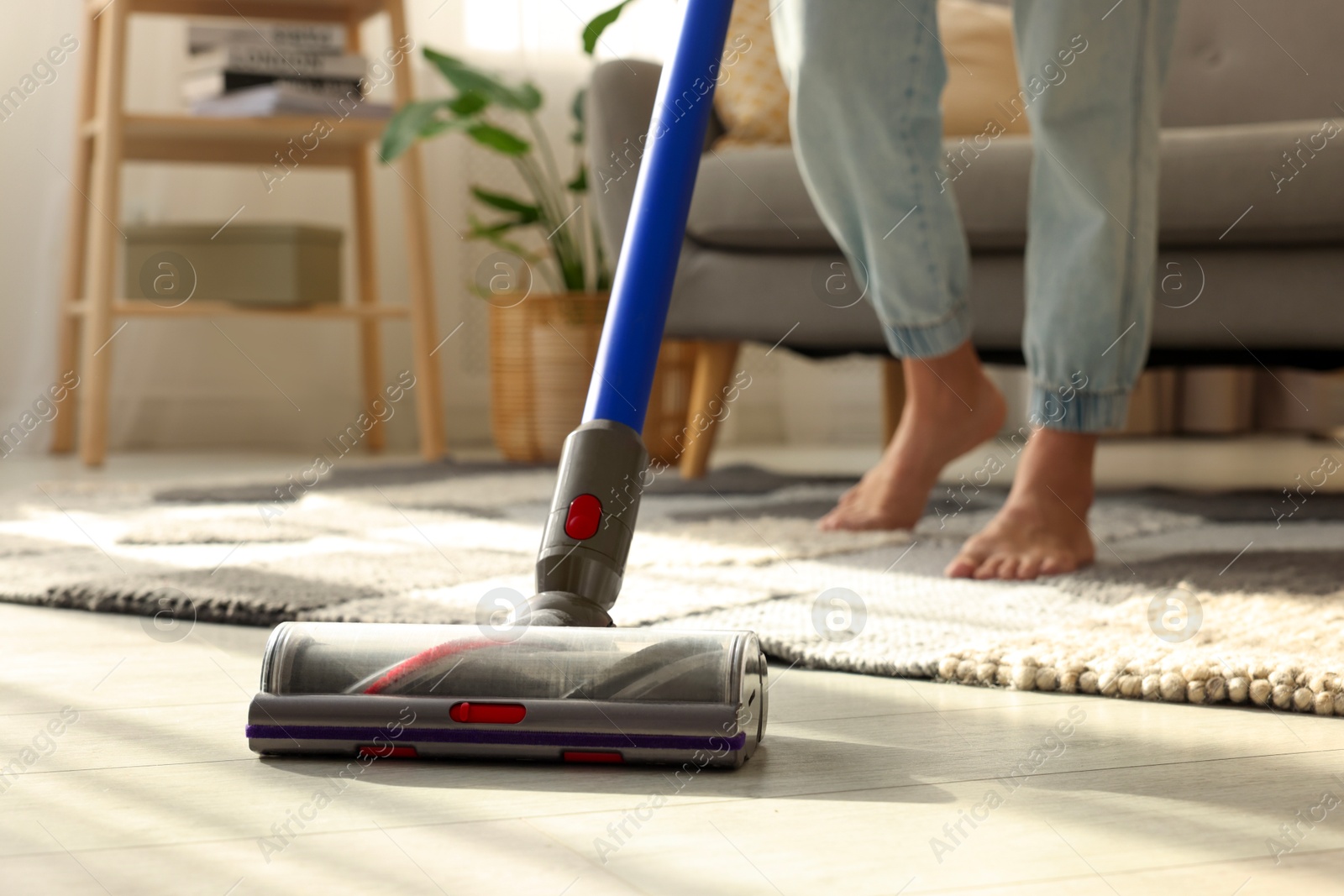 Photo of Woman cleaning floor with cordless vacuum cleaner at home, closeup