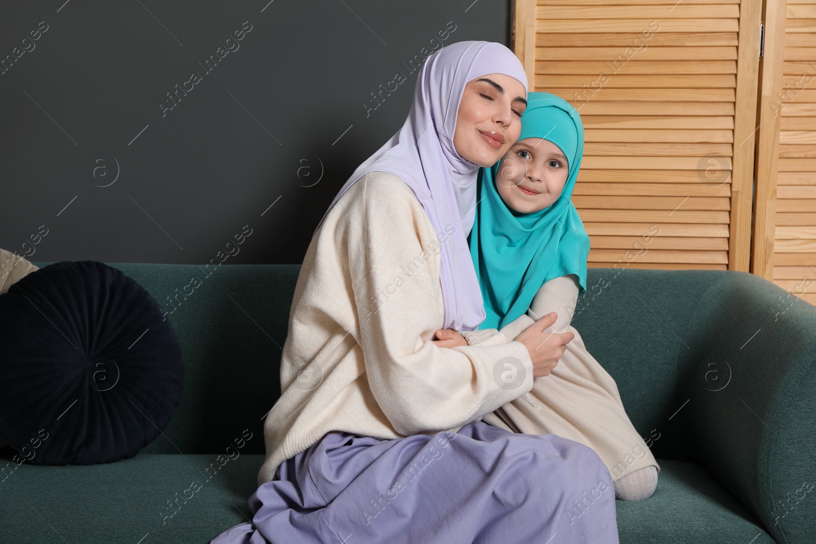 Photo of Muslim woman and her daughter sitting on sofa at home