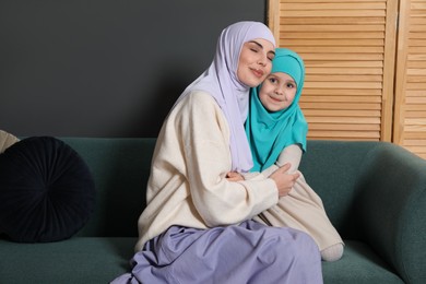 Photo of Muslim woman and her daughter sitting on sofa at home