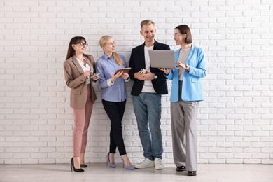 Photo of Group of people using different gadgets near white brick wall indoors. Modern technology