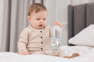 Photo of Cute little baby with money in bottle on bed at home