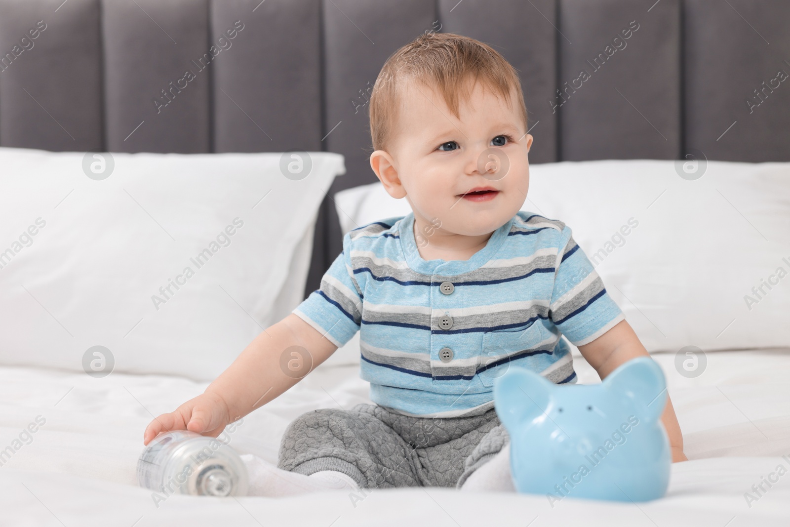 Photo of Cute little baby with money in bottle and piggybank on bed at home