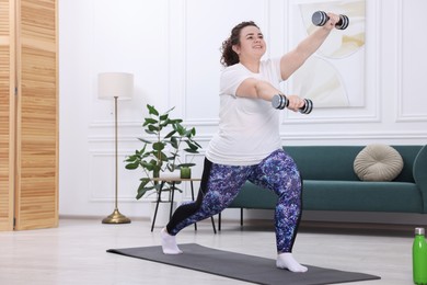 Photo of Plus size woman with dumbbells training at home