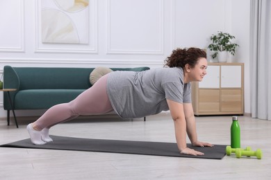 Photo of Woman doing plank exercise on fitness mat at home