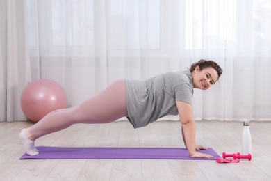 Photo of Woman doing plank exercise on fitness mat at home