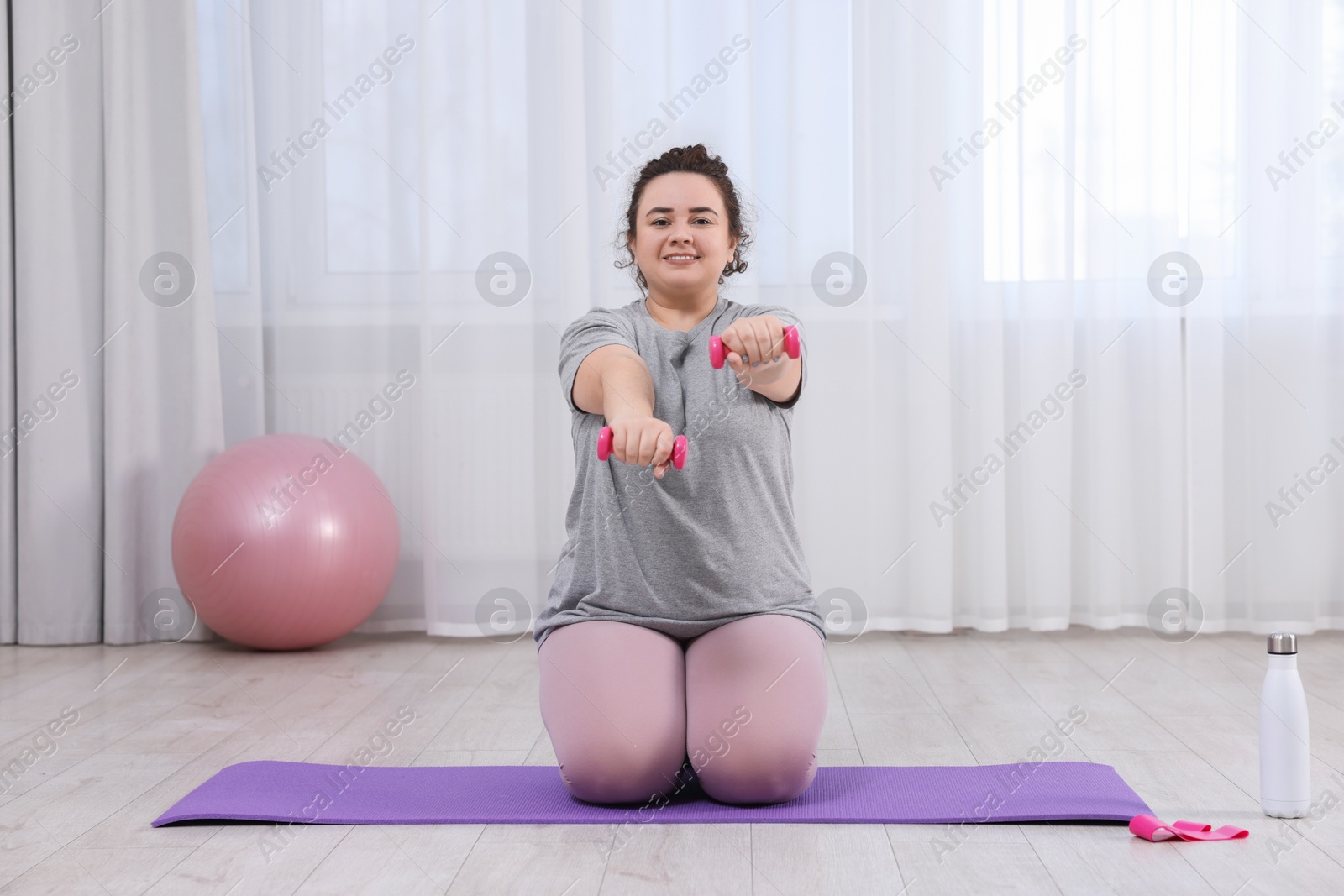 Photo of Plus size woman with dumbbells training at home