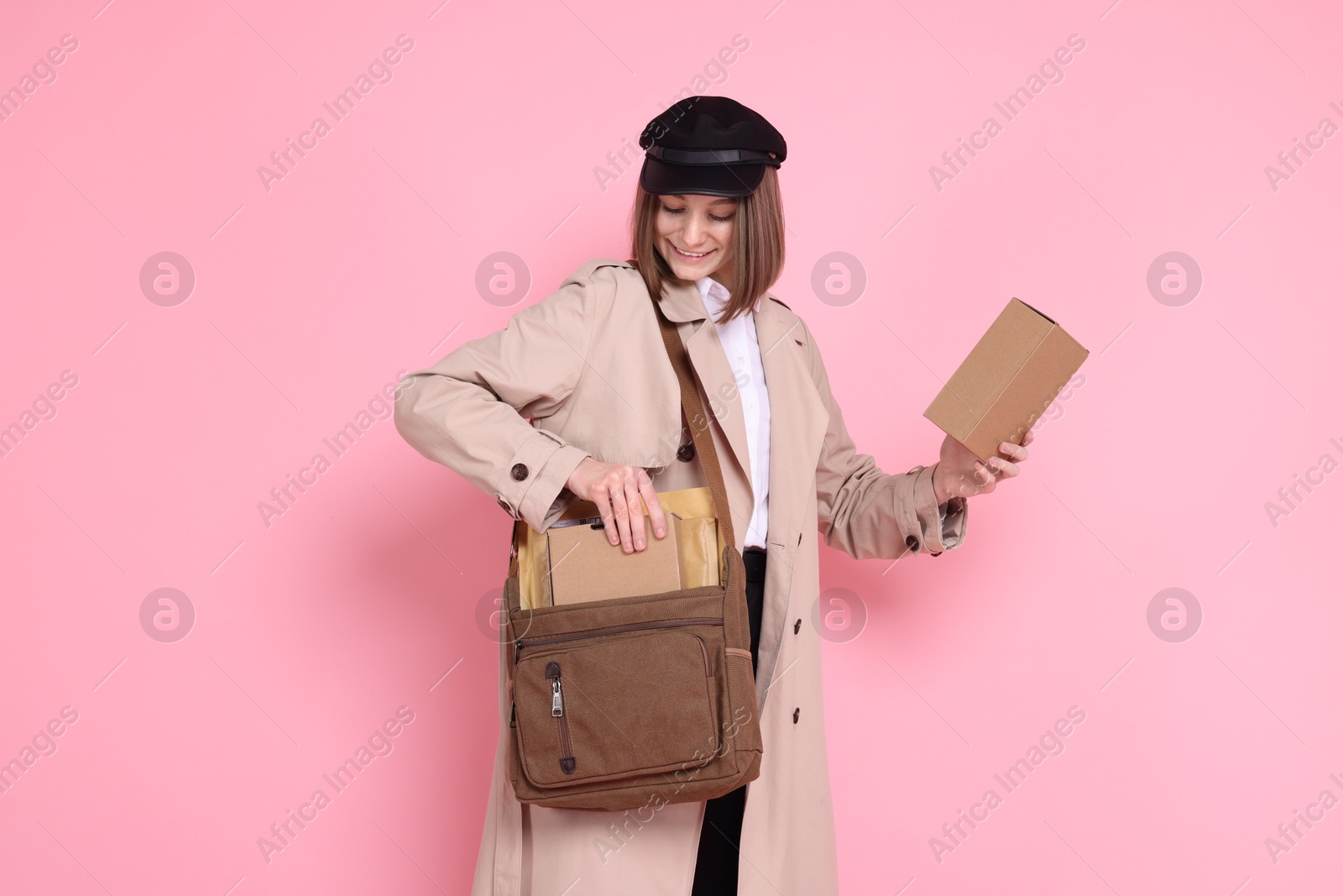 Photo of Happy postwoman with bag and parcels on pink background