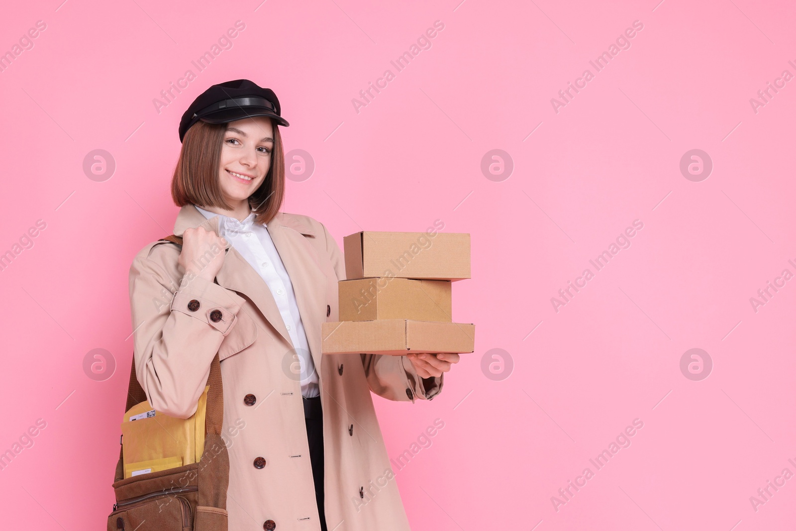 Photo of Happy postwoman with bag and parcels on pink background. Space for text