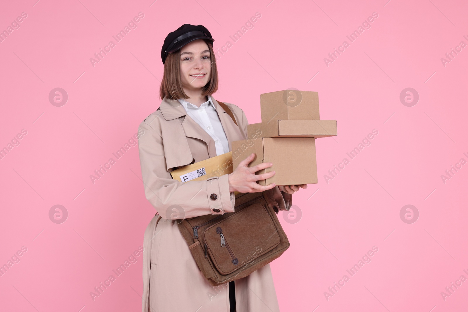 Photo of Happy postwoman with bag and parcels on pink background