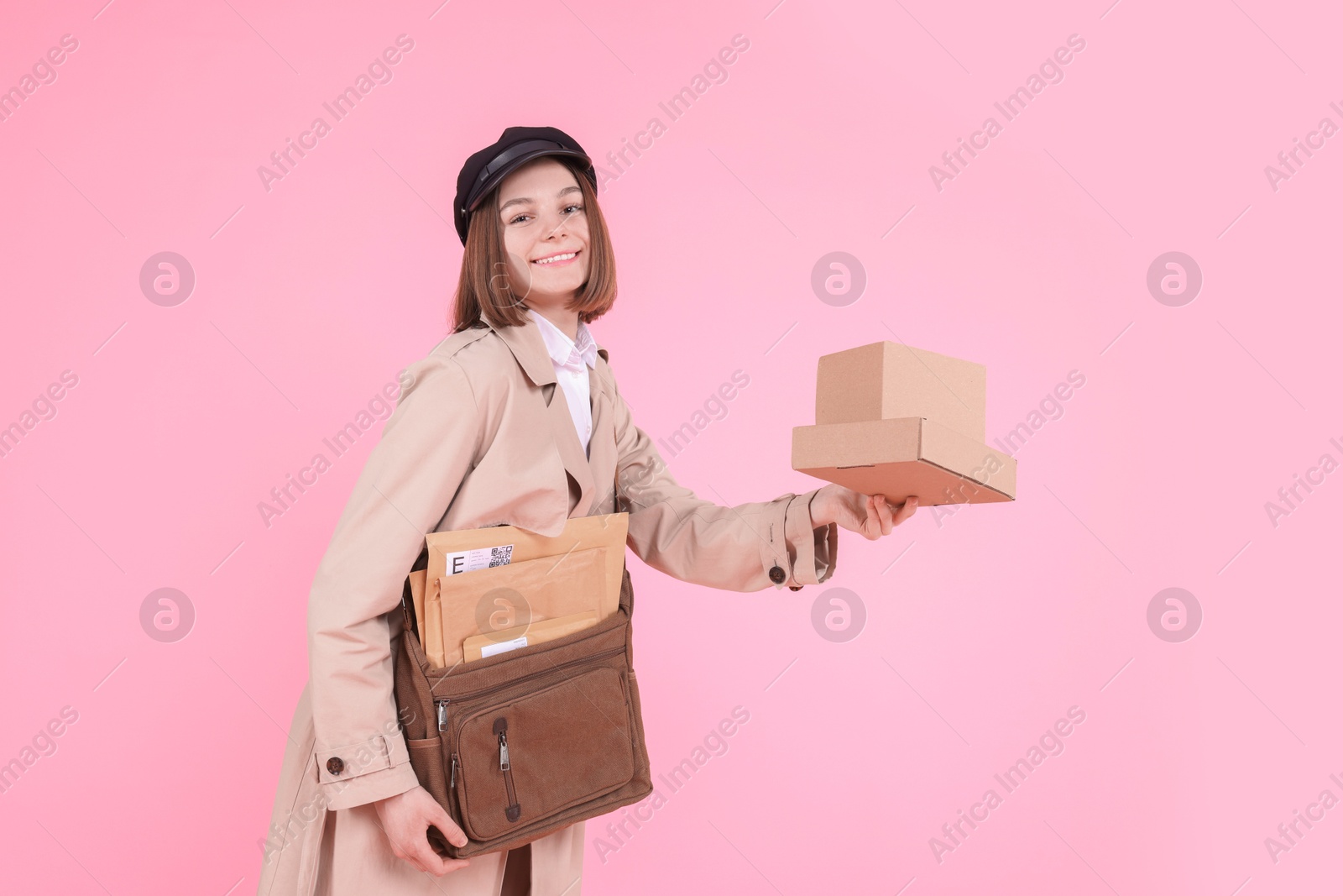 Photo of Happy postwoman with bag and parcels on pink background