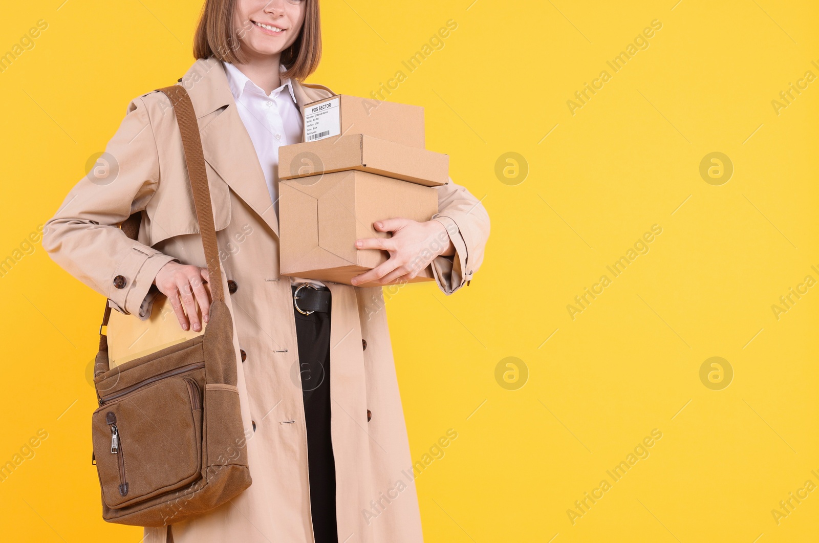 Photo of Happy postwoman with bag and parcels on yellow background, closeup. Space for text