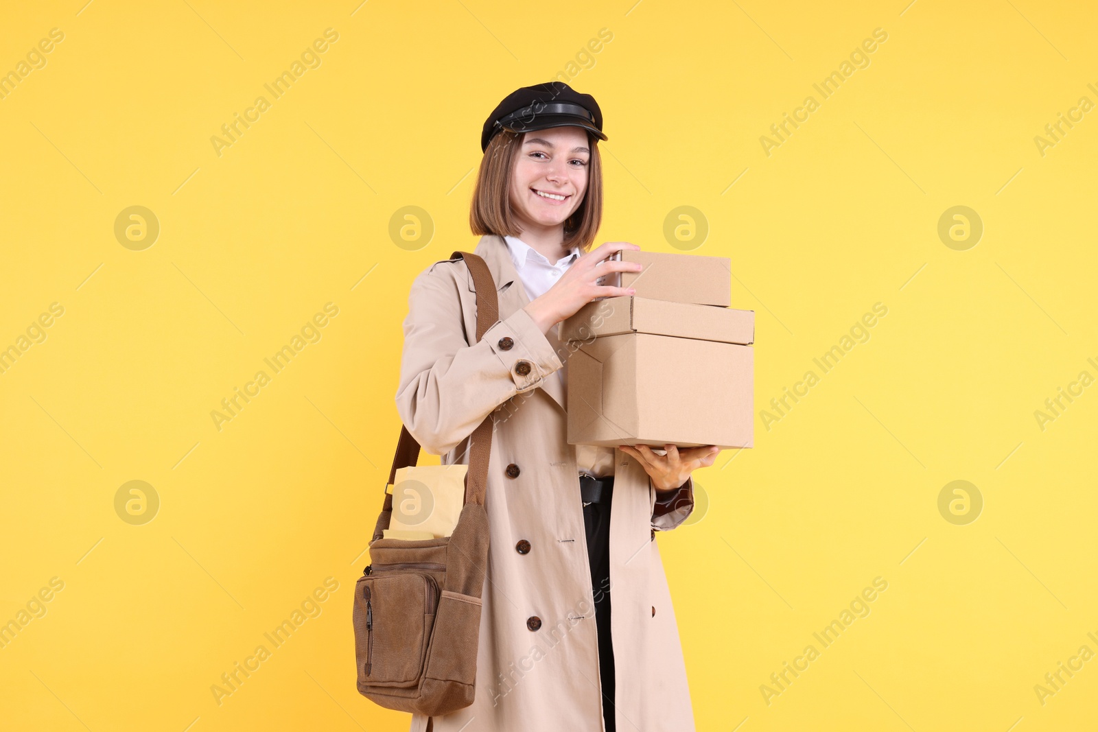 Photo of Happy postwoman with bag and parcels on yellow background