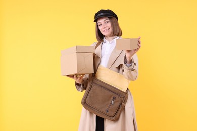 Photo of Happy postwoman with bag and parcels on yellow background