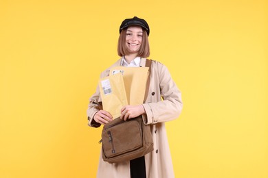 Photo of Happy postwoman with bag and envelopes on yellow background