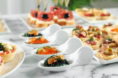 Photo of Many different tasty canapes on white marble table, closeup