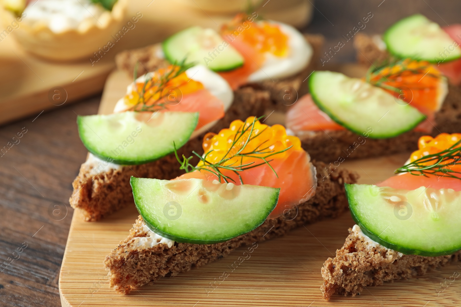 Photo of Tasty canapes with salmon and cucumber on wooden table, closeup