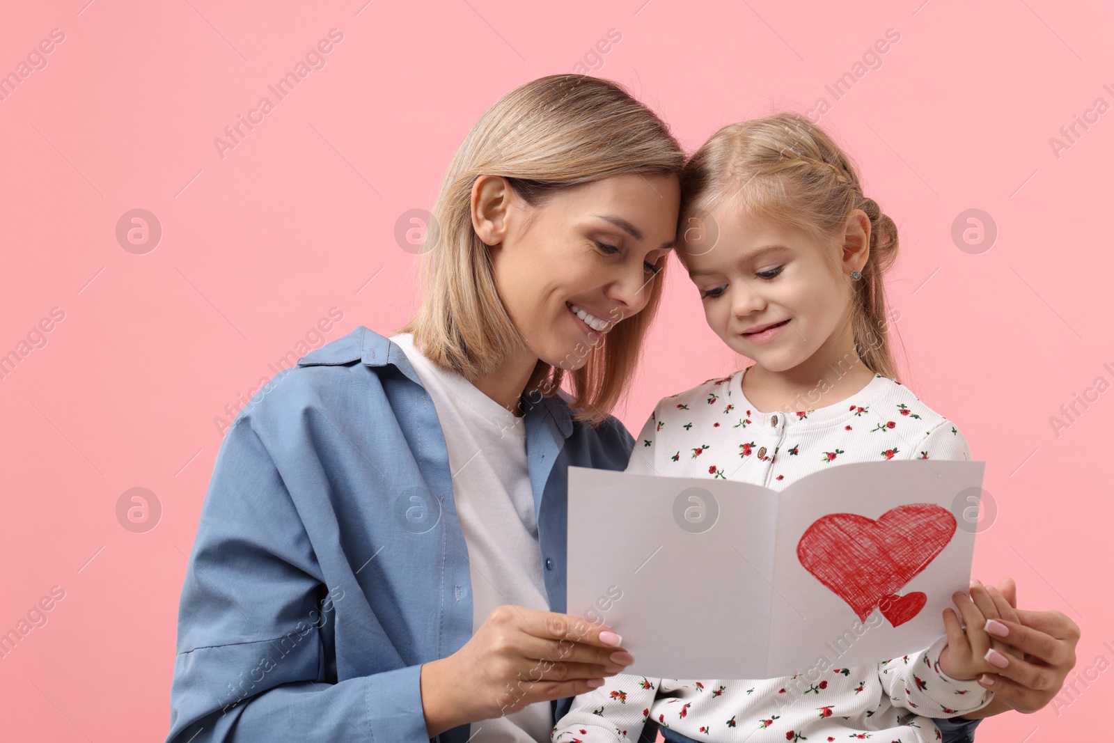 Photo of Happy woman with her daughter and greeting card on pink background. Mother's Day celebration