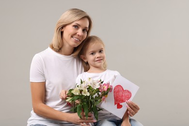 Photo of Happy woman with her daughter, bouquet of alstroemeria flowers and greeting card on gray background. Mother's Day celebration