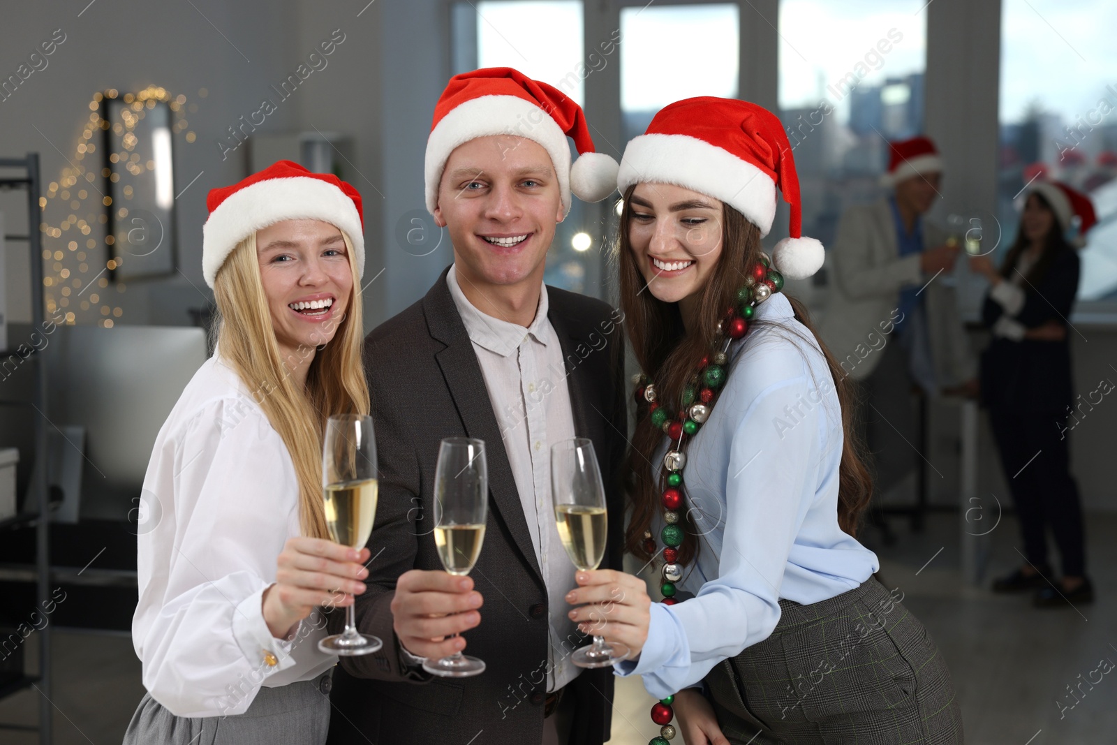 Photo of Cheerful coworkers in Santa hats with glasses of wine at office Christmas party