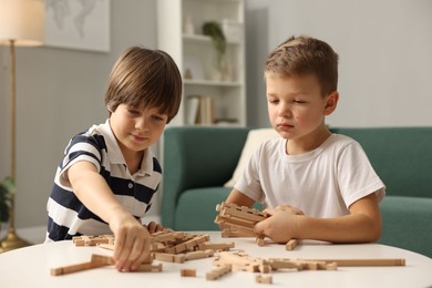 Photo of Cute brothers playing with wooden construction set at table indoors