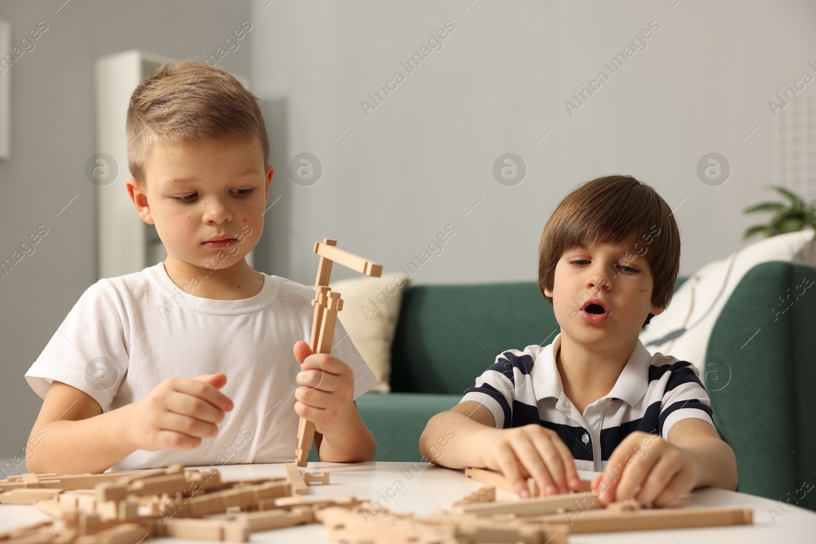 Photo of Cute brothers playing with wooden construction set at table indoors