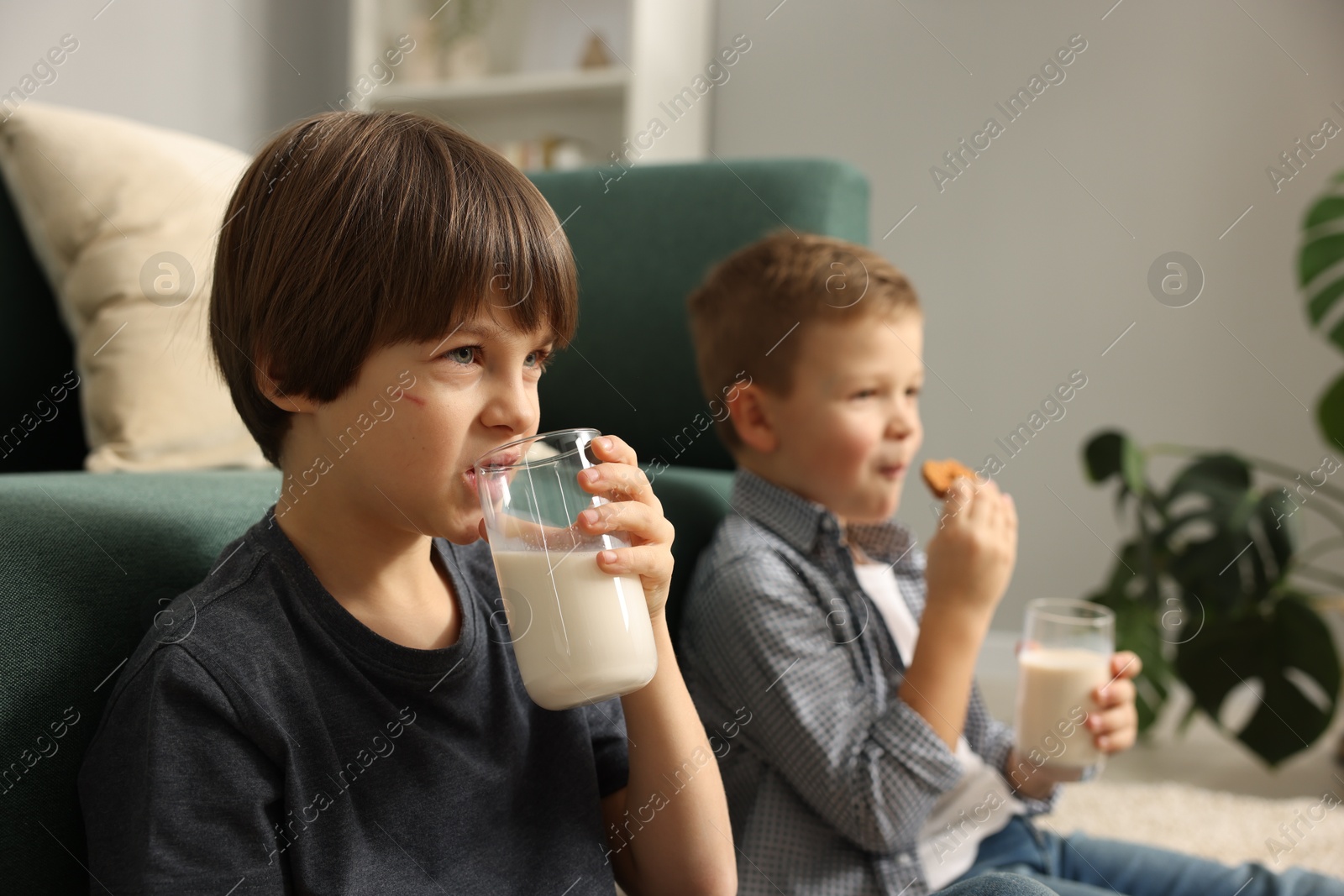 Photo of Cute brothers with glasses of milk and cookies at home, selective focus