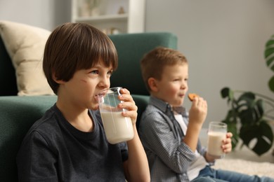 Photo of Cute brothers with glasses of milk and cookies at home, selective focus