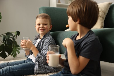 Photo of Cute brothers with glasses of milk on floor at home