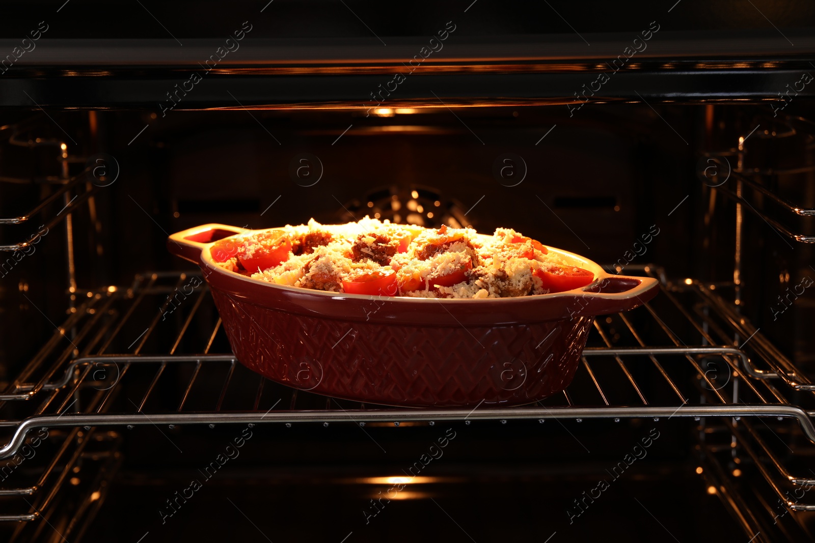 Photo of Uncooked pasta casserole with cheese, tomatoes and minced meat in baking dish in oven, closeup