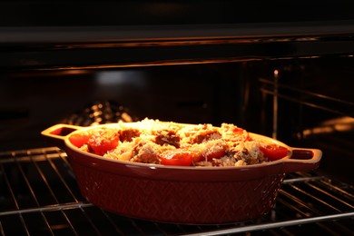 Photo of Uncooked pasta casserole with cheese, tomatoes and minced meat in baking dish in oven, closeup