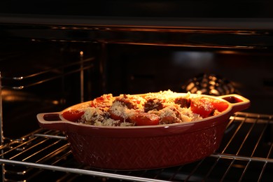 Photo of Uncooked pasta casserole with cheese, tomatoes and minced meat in baking dish in oven, closeup