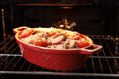 Photo of Uncooked pasta casserole with cheese, tomatoes and minced meat in baking dish in oven, closeup