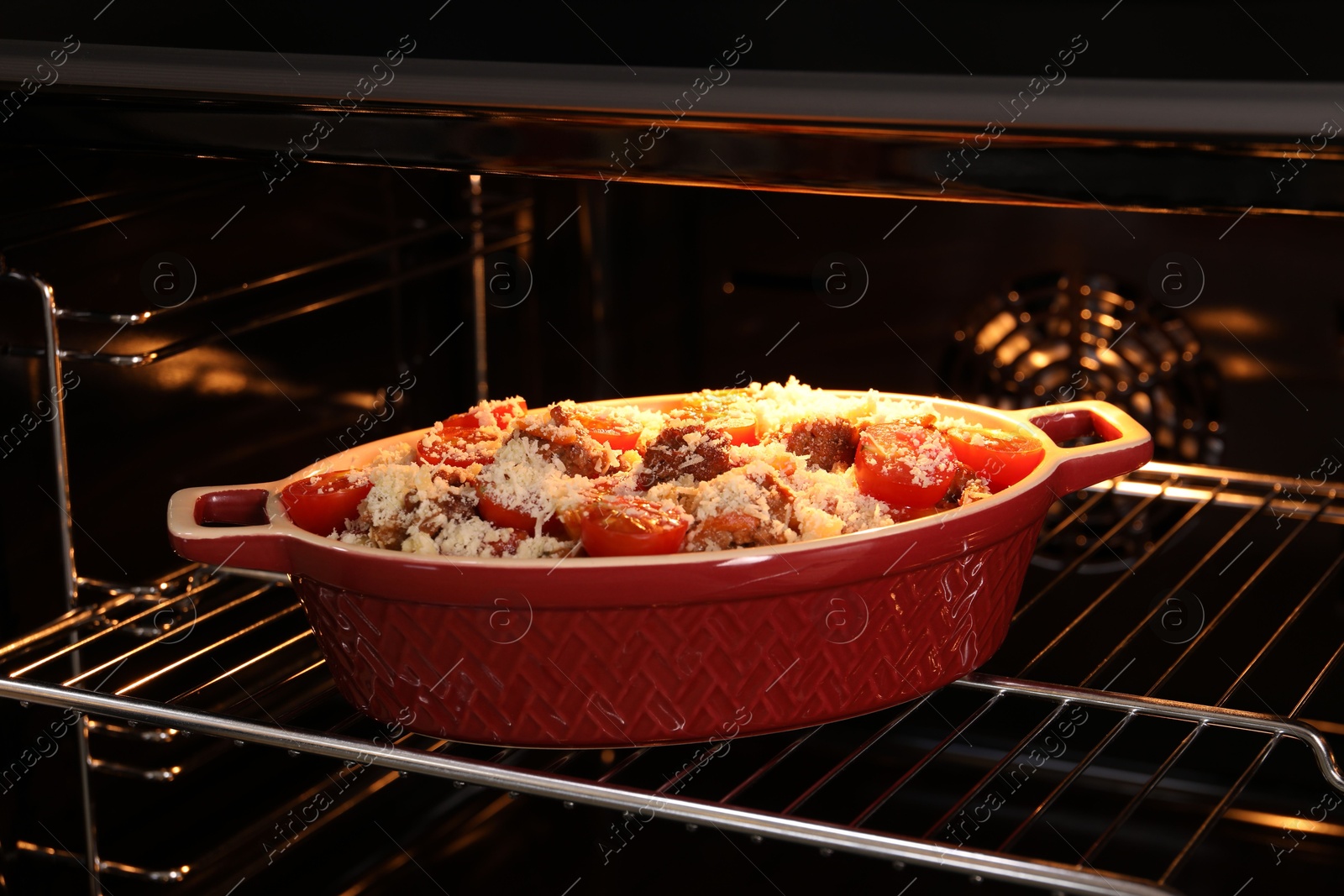 Photo of Uncooked pasta casserole with cheese, tomatoes and minced meat in baking dish in oven, closeup