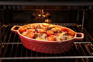 Photo of Delicious pasta casserole with cheese, tomatoes and minced meat in baking dish in oven, closeup