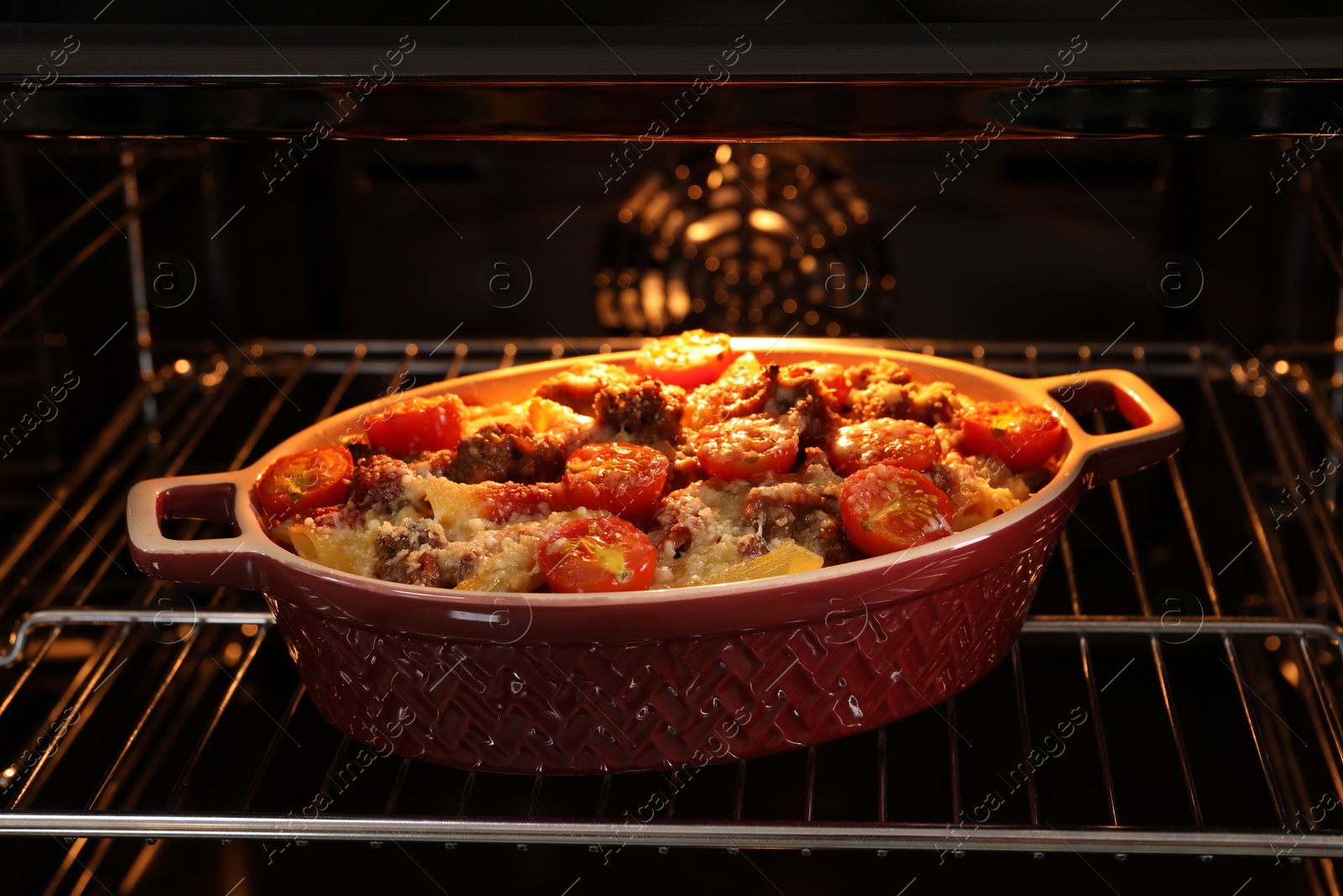 Photo of Delicious pasta casserole with cheese, tomatoes and minced meat in baking dish in oven, closeup