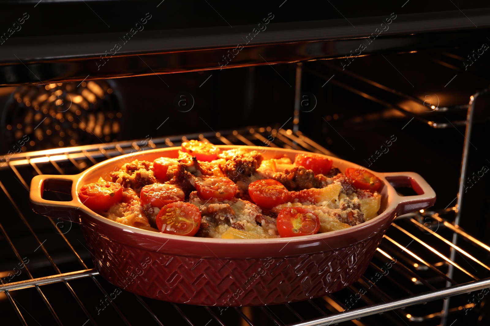 Photo of Delicious pasta casserole with cheese, tomatoes and minced meat in baking dish in oven, closeup