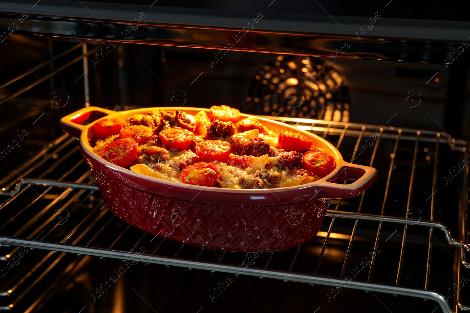 Photo of Delicious pasta casserole with cheese, tomatoes and minced meat in baking dish in oven, closeup