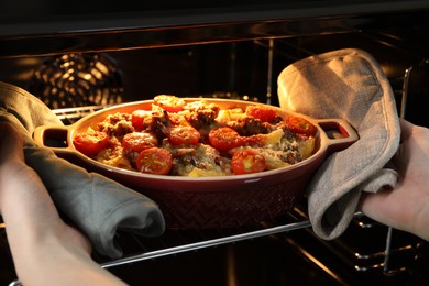 Photo of Woman taking delicious pasta casserole with cheese, tomatoes and minced meat out of oven, closeup