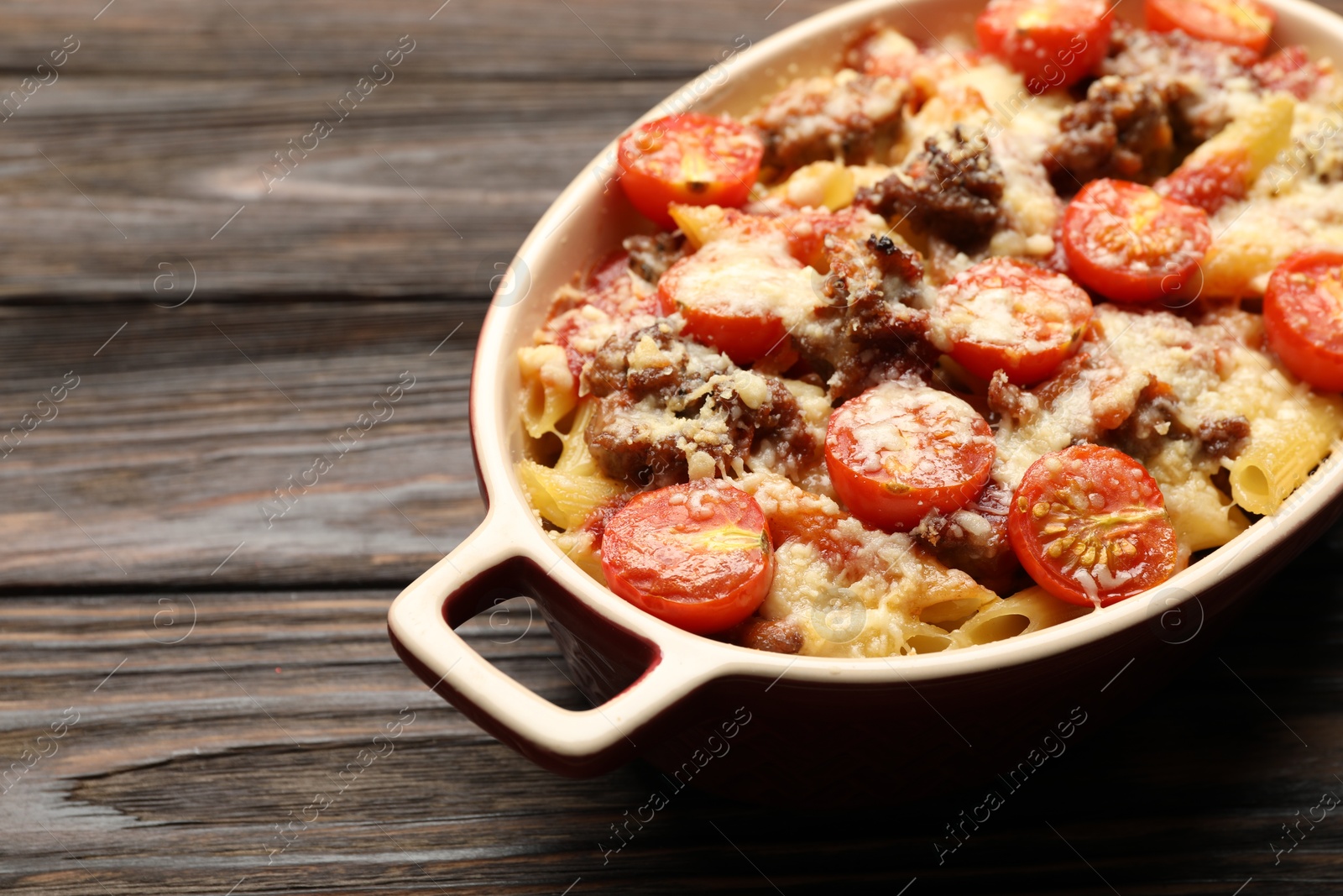 Photo of Delicious pasta casserole with cheese, tomatoes and minced meat in baking dish on wooden table, closeup. Space for text