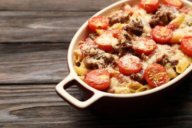 Photo of Delicious pasta casserole with cheese, tomatoes and minced meat in baking dish on wooden table, closeup. Space for text