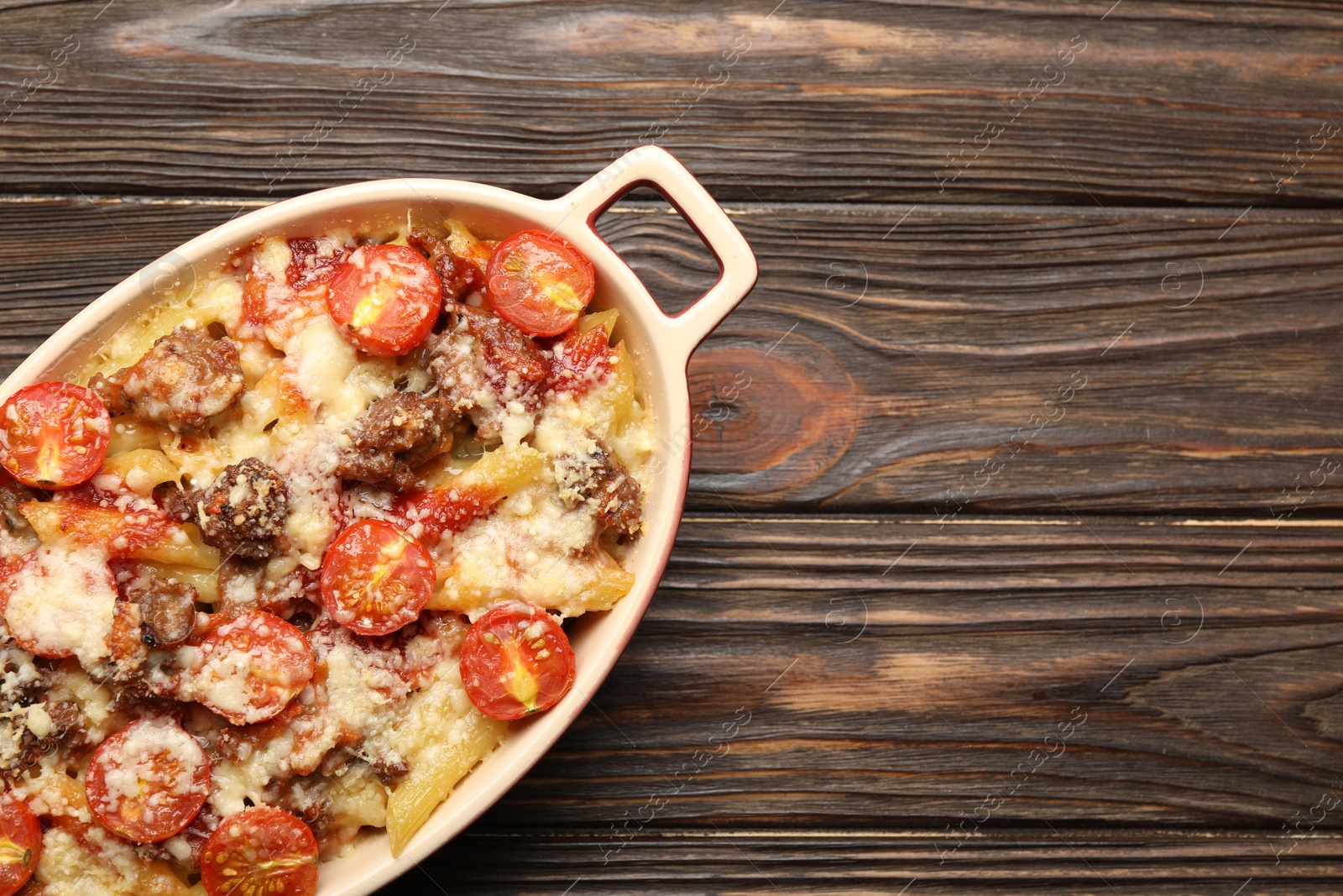 Photo of Delicious pasta casserole with cheese, tomatoes and minced meat in baking dish on wooden table, top view. Space for text