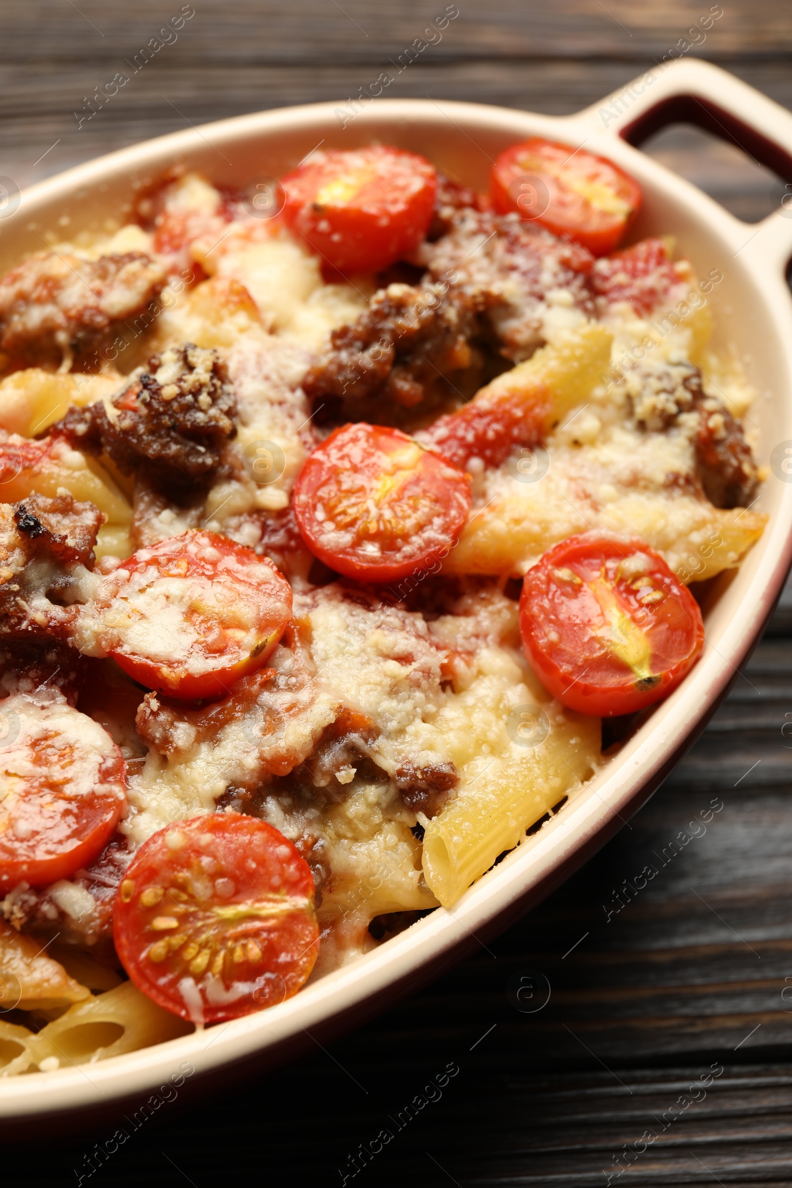 Photo of Delicious pasta casserole with cheese, tomatoes and minced meat in baking dish on wooden table, closeup