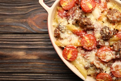 Photo of Delicious pasta casserole with cheese, tomatoes and minced meat in baking dish on wooden table, top view. Space for text