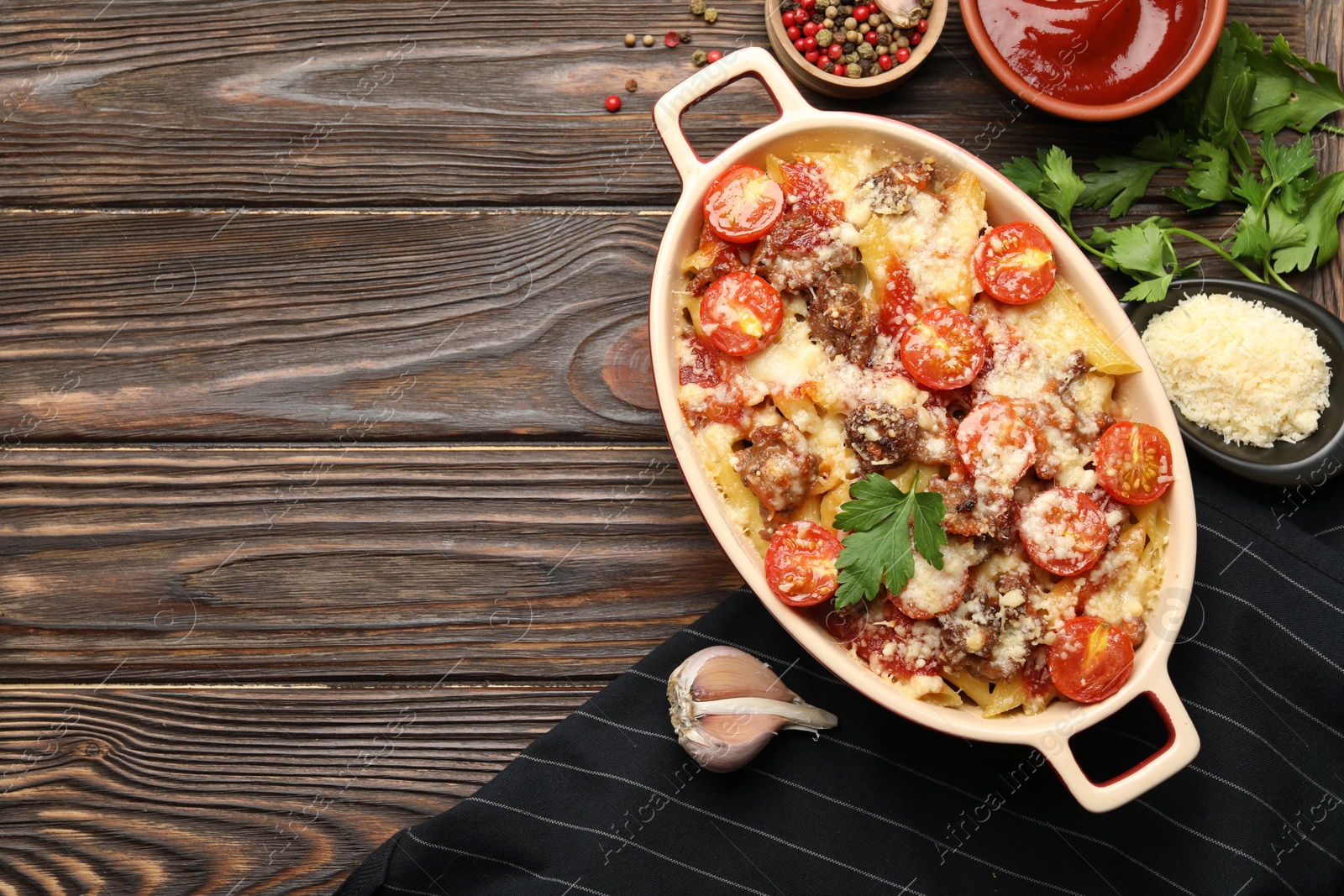 Photo of Delicious pasta casserole in baking dish with ingredients and sauce on wooden table, flat lay. Space for text