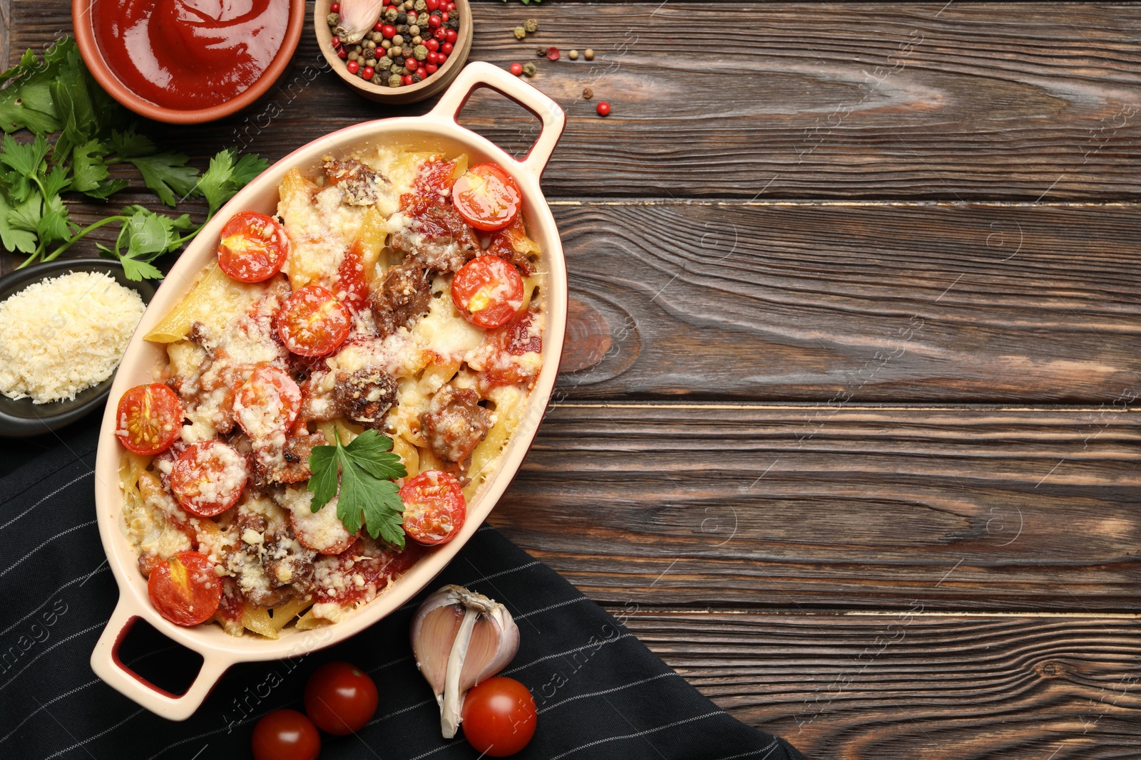 Photo of Delicious pasta casserole in baking dish with ingredients and sauce on wooden table, flat lay. Space for text